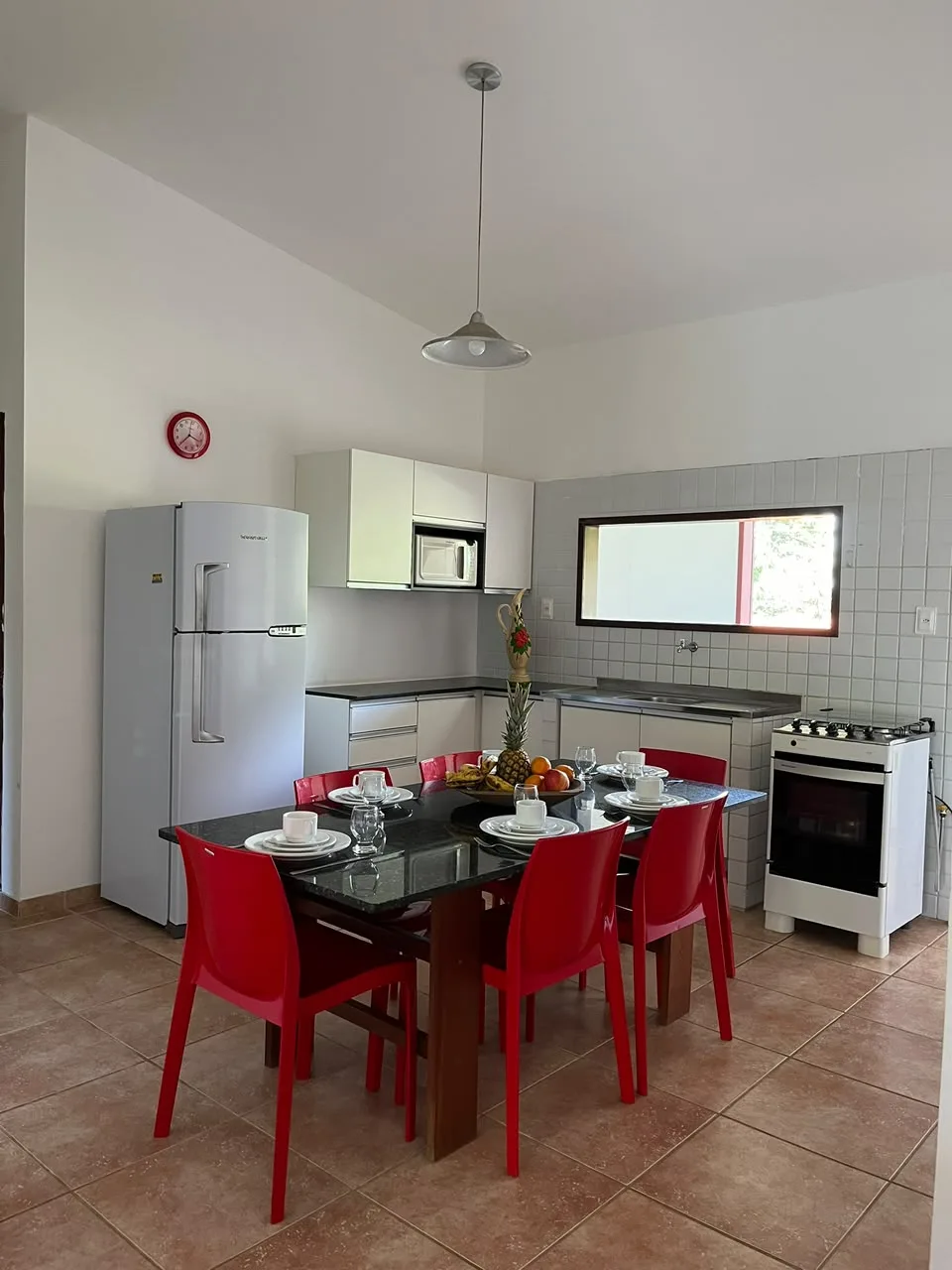 Cozinha com geladeira, fogão e mesa posta com cadeiras vermelhas