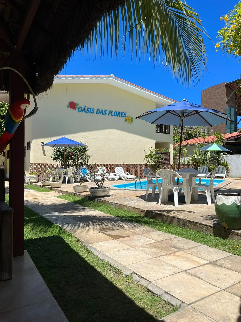 Jardim de entrada com a fachada do Oásis das Flores e a piscina ao fundo